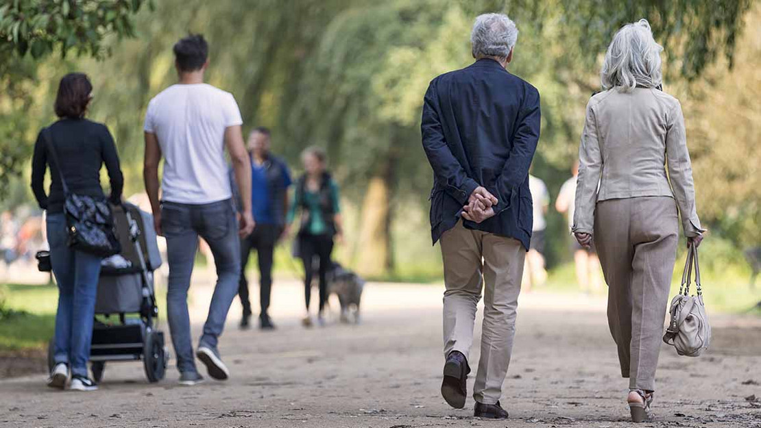 Älteres Ehepaar und junge Eltern mit Kinderwagen gehen in einem Park spazieren. 