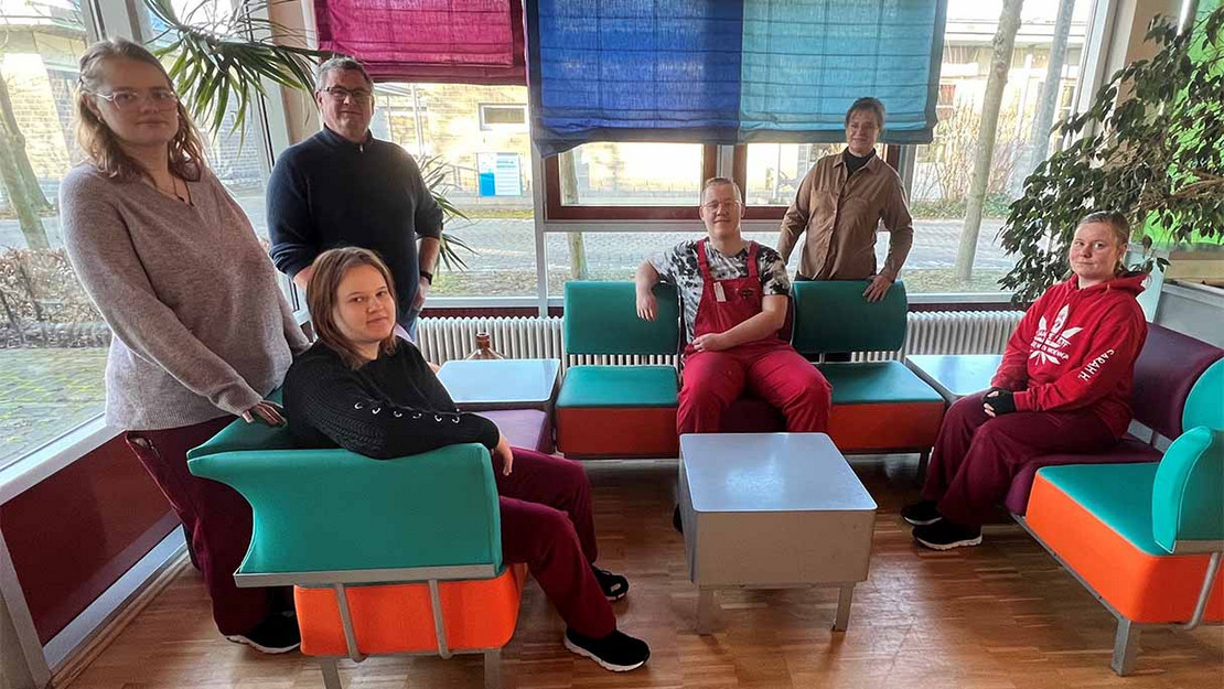 Junge Leute und zwei Erwachsenen neben bunten Möbelstücken. 