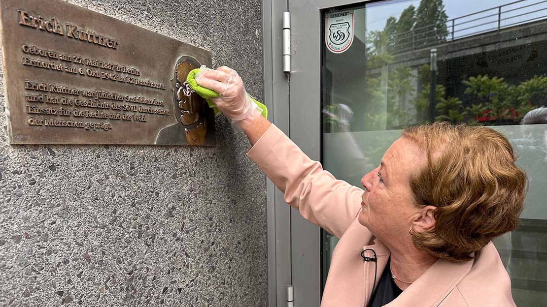 Eine Frau putzt eine Plakette an der Wand neben der Eingangstür der SoVD-Bundesgeschäftsstelle. 