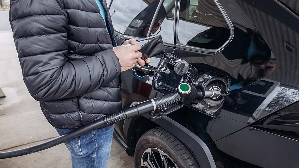 Ein Mann tankt sein Auto und öffnet sein Portemonnaie. 