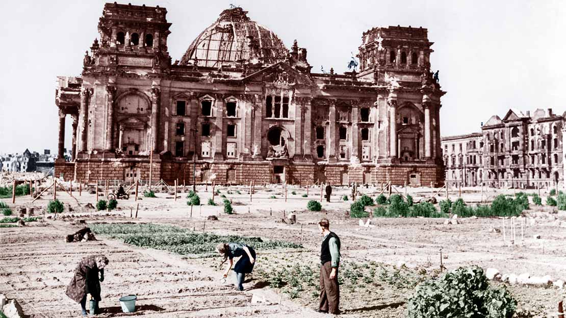 Menschen gärtnern vor dem zerbombten Reichstag. 